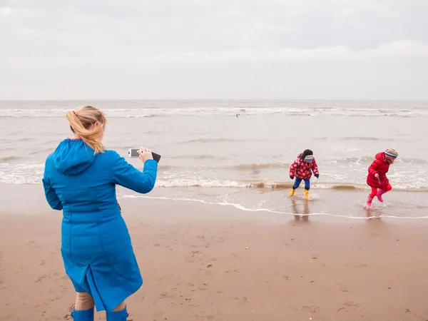 Bir kadın ve iki küçük çocuk kış sahilde oynarken — Stok fotoğraf