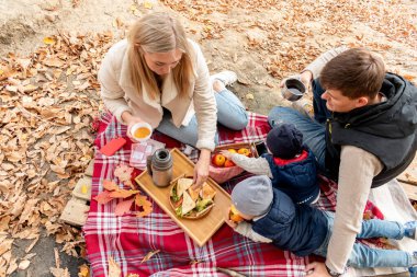 Ailesi göl kenarındaki ormanda dinlenirken piknik yapmış. Aile bireyi bakım konsepti. Sonbahar manzarası. İnsanların çeşitliliği