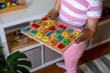 Çocuk raftan ahşap harfleri alıyor. İngiliz alfabesi. Montessori kumaşı. Evde eğitim kavramı. Çevre dostu oyuncak