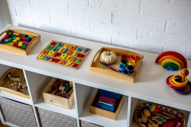 Çocuk odasında sepet ve çekmeceli beyaz raf. Montessori kumaşı. Evde eğitim kavramı. Çevre dostu oyuncak