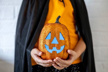 Cadı kostümü giymiş bir kız elinde parlak bir balkabağı tutuyor. Cadılar Bayramı konsepti. Boşluğu kopyala.