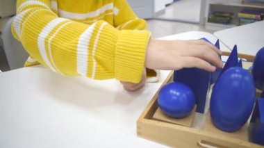 Montessori okulunda kızların eli renkli ahşap geometrik şekiller bulmacası çözüyor. Matematiksel geometri kullanma kavramı çocuk eğitimi için kaynak öğrenme kavramı.