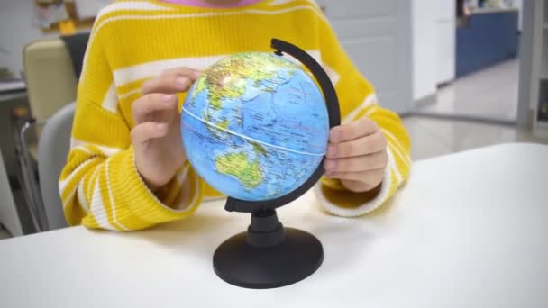 縞模様の黄色いセーターの少女は モンテッソーリ学校の大陸の惑星地球で指を指しています 教育のための地球を使用する概念子供の地理と構造地球 — ストック動画