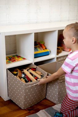 Children pulls out a box of toys. Educational toys for young children. Little boy wants to play construction set on the brown floor at home or in kindergarten.