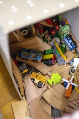 Children pull out wooden railway from a toy box. Educational toys for young children. Little boy wants to play construction set on the brown floor at home or in kindergarten.