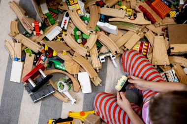 Kids play with wooden railway. Child with toy train. Cute kid playing cars and engine. Educational toys for young children. Little boy building railroad tracks on brown floor at home or kindergarten.