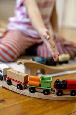Kids play with wooden railway. Child with toy train. Cute kid playing cars and engine. Educational toys for young children. Little boy building railroad tracks on brown floor at home or kindergarten.