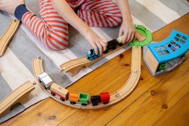 Kids play with wooden railway. Child with toy train. Cute kid playing cars and engine. Educational toys for young children. Little boy building railroad tracks on brown floor at home or kindergarten.