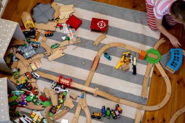 Kids play with wooden railway. Child with toy train. Cute kid playing cars and engine. Educational toys for young children. Little boy building railroad tracks on brown floor at home or kindergarten.