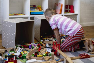 Kids play with wooden railway. Child with toy train. Cute kid playing cars and engine. Educational toys for young children. Little boy building railroad tracks on brown floor at home or kindergarten.