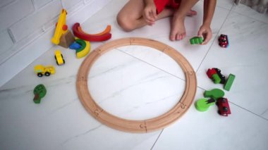 Çocuklar ahşap demiryolu ile oynarlar. Oyuncak trenli çocuk. Araba ve motor çalan sevimli bir çocuk. Küçük çocuklar için eğitici oyuncaklar. Küçük çocuk beyaz zemine tren rayları inşa ediyor..