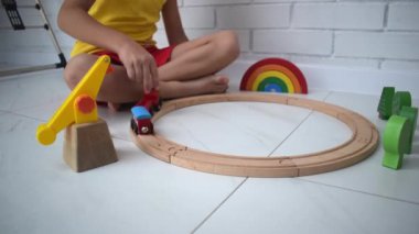 Çocuklar ahşap demiryolu ile oynarlar. Oyuncak trenli çocuk. Araba ve motor çalan sevimli bir çocuk. Küçük çocuklar için eğitici oyuncaklar. Küçük çocuk beyaz zemine tren rayları inşa ediyor..