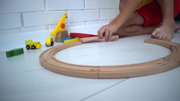 孩子们玩木制铁路 玩玩具火车的孩子可爱的孩子玩汽车和引擎 幼儿教育玩具 小男孩在家里或幼儿园的白色地板上建造铁路轨道 — 图库视频影像