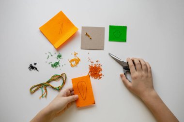 Child girl weaves a brooch from beads. Handmade. Favorite hobby. Diy process