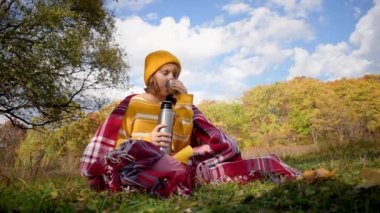 Close-up girl hiking traveler drinking hot tea and relaxing in the fall forest on sunny autumn day. Health care, authenticity, sense of balance and calmness. Slow motion video.