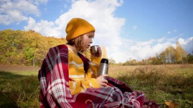 Close-up girl hiking traveler drinking hot tea and relaxing in the fall forest on sunny autumn day. Health care, authenticity, sense of balance and calmness. Slow motion video.