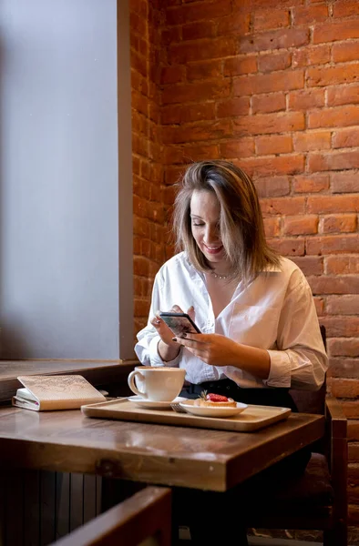 Genç bir kadın kahve içerken cep telefonundan mesaj yazıyor. İş kadını sosyal mesafeyi koruyor ve uzaktan çalışıyor. Yeni normal kavram