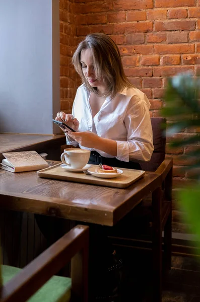 Genç bir kadın kahve içerken cep telefonundan mesaj yazıyor. İş kadını sosyal mesafeyi koruyor ve uzaktan çalışıyor. Yeni normal kavram