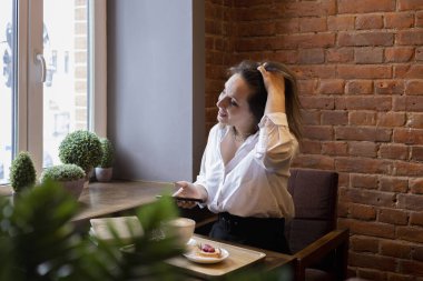 Genç bir kadın kahve içerken cep telefonundan mesaj yazıyor. İş kadını sosyal mesafeyi koruyor ve uzaktan çalışıyor. Yeni normal kavram