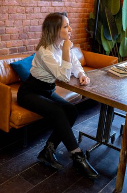 Genç kadın kanepedeki bir masada bir kafede oturuyor. Kahvaltıyı bekliyorum. Mola sırasında mahremiyet.