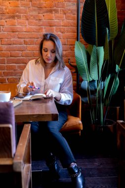 Genç kadın kanepedeki bir masada bir kafede oturuyor. Kahvaltıyı bekliyorum. Mola sırasında mahremiyet.