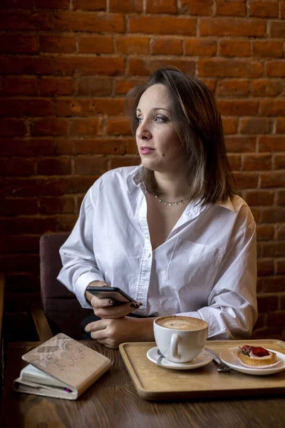 Kadın takım elbiseli bir kadın elinde bir telefon tutuyor ve pencereden dışarı bakıyor. Yemek molası. Ofis çalışanı.