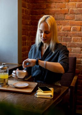 Genç iş kadını bir kafede oturuyor ve akıllı saatine bakıyor. Yemek molası. Modern teknoloji kavramı