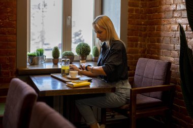 Genç iş kadını bir kafede oturuyor ve akıllı saatine bakıyor. Yemek molası. Modern teknoloji kavramı