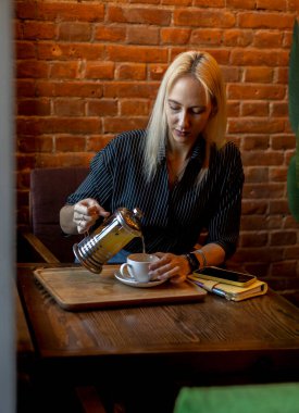 Çaydanlığı tutan ve beyaz fincana çay dolduran bir kadının eli. İş kadını mesaiden sonra hafif bir çay saati geçiriyor. Antioksidanlı yeşil bitki