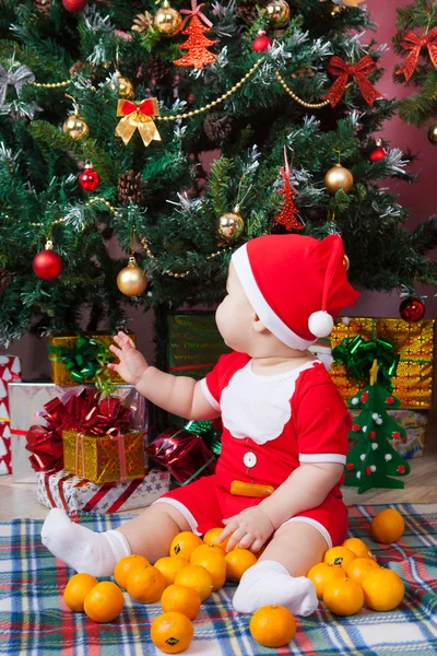 Baby in santa kostuum in de buurt van een kerstboom — Stockfoto