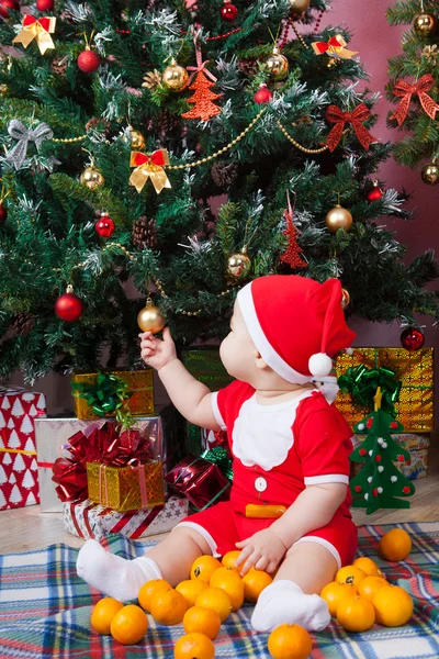 Baby in santa kostuum in de buurt van een kerstboom — Stockfoto