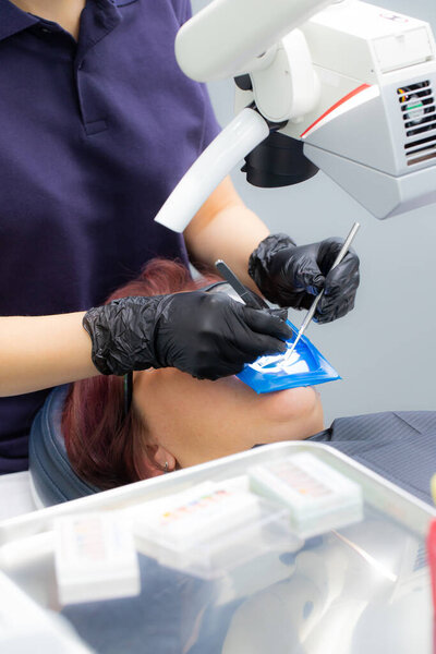 woman dentist treats root canals using a microscope in a dental clinic. Woman patient lying on dentist chair with open mouth with latex protective napkin