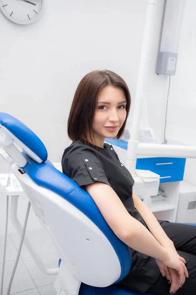 Молодая женщина дантист сидит в своем медицинском кабинете в черном костюме — стоковое фото