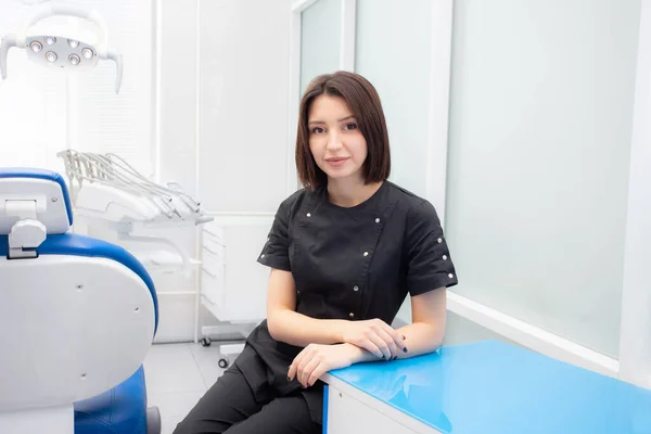 Uma jovem dentista está sentada em seu consultório médico em um terno preto Fotografias De Stock Royalty-Free