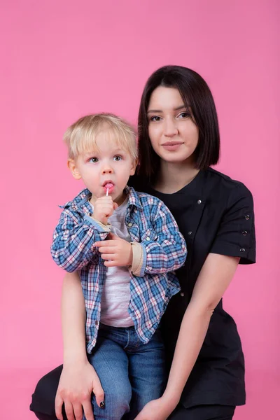 Mujer pediatra joven con un lindo bebé sobre un fondo rosa. chico con caramelo — Foto de Stock