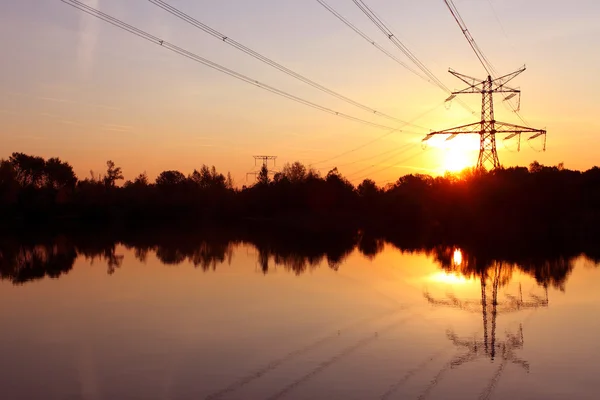 Pylon energii elektrycznej z odbiciem w wodzie na zachodzie słońca — Zdjęcie stockowe