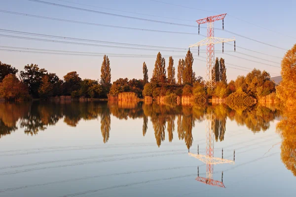 Hoogspanningsmast met weerspiegeling in water bij zonsondergang — Stockfoto