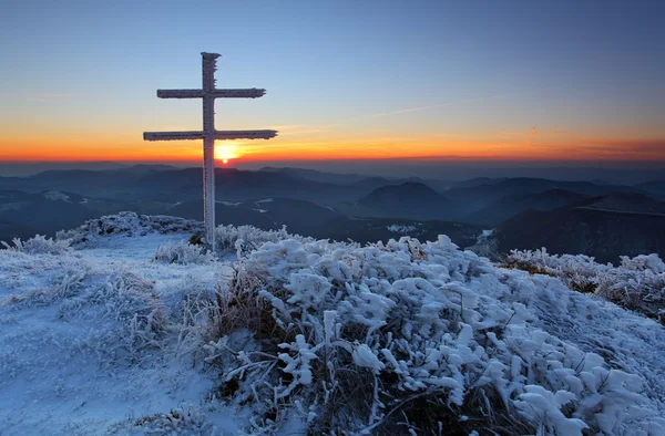 A frosty sunset in mountains with cross — Stock Photo, Image
