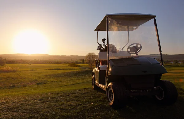 Carro de golf sobre verde agradable y puesta de sol — Foto de Stock