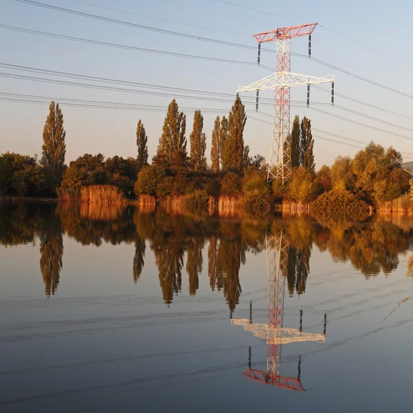 Electricity pylon with reflection in water at sunset — Stock Photo, Image