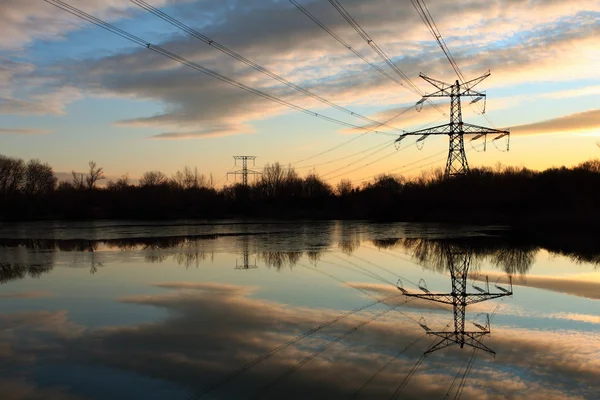 Gün batımında suda yansıması ile elektrik pilon — Stok fotoğraf
