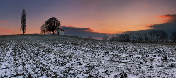 Západ slunce na zmrzlé pole s kaplí. — Stock fotografie