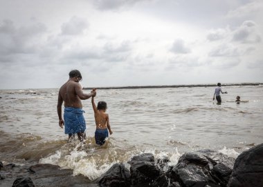 Mumbai,India-07-30-2022:people and children venturing dangerously in haji ali poluted sea waters during high tides risking their lives