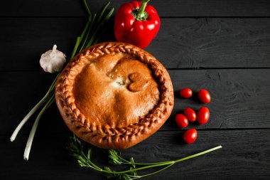 Round pie on a black wooden background. Composition with ingredients. With a copy space.
