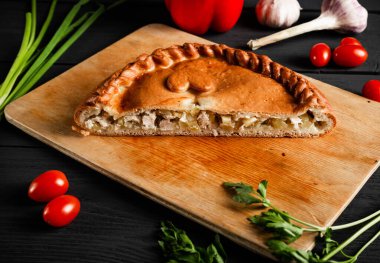 Kesme tahtasında etli ve patatesli turta. İçeriği olan siyah bir arkaplanda kompozisyon.