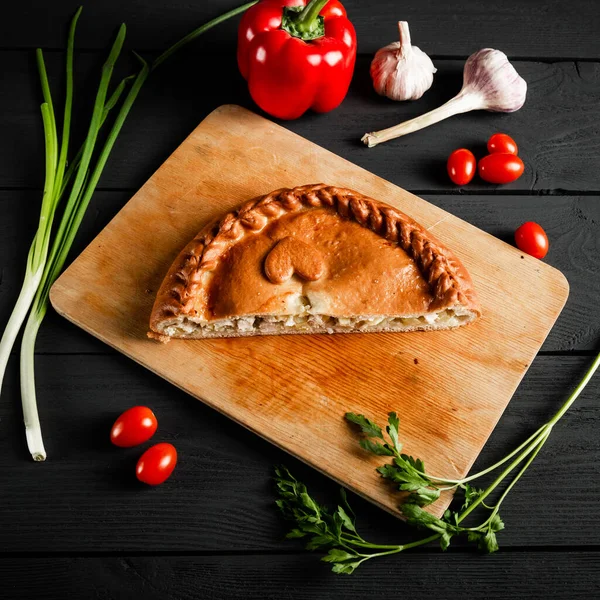 Kesme tahtasında etli ve patatesli turta. İçeriği olan siyah bir arkaplanda kompozisyon.