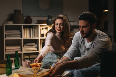 Arkadaşlar evde bira içip pizza yiyorlar.