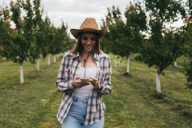 Kadın çiftçi meyve bahçesinde akıllı telefon kullanıyor.