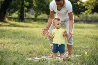 Anne ve oğlu halka açık bir parkta oynuyorlar. yürümeyi öğrenmek