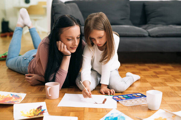 mother and her daughter painting with water colors at home